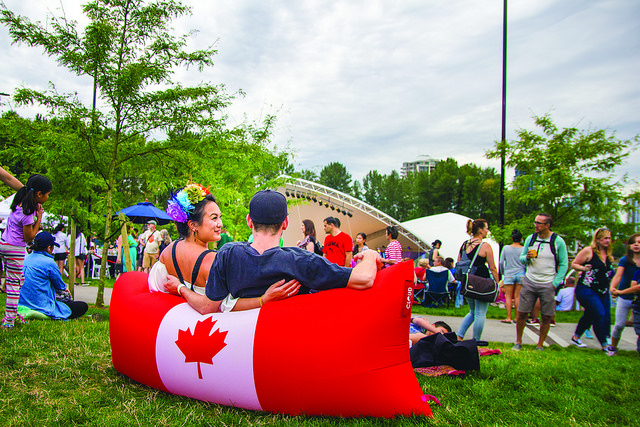 Coquitlam Canada Day-市中心公园有两个人坐在充气枕头椅上，带有加拿大国旗